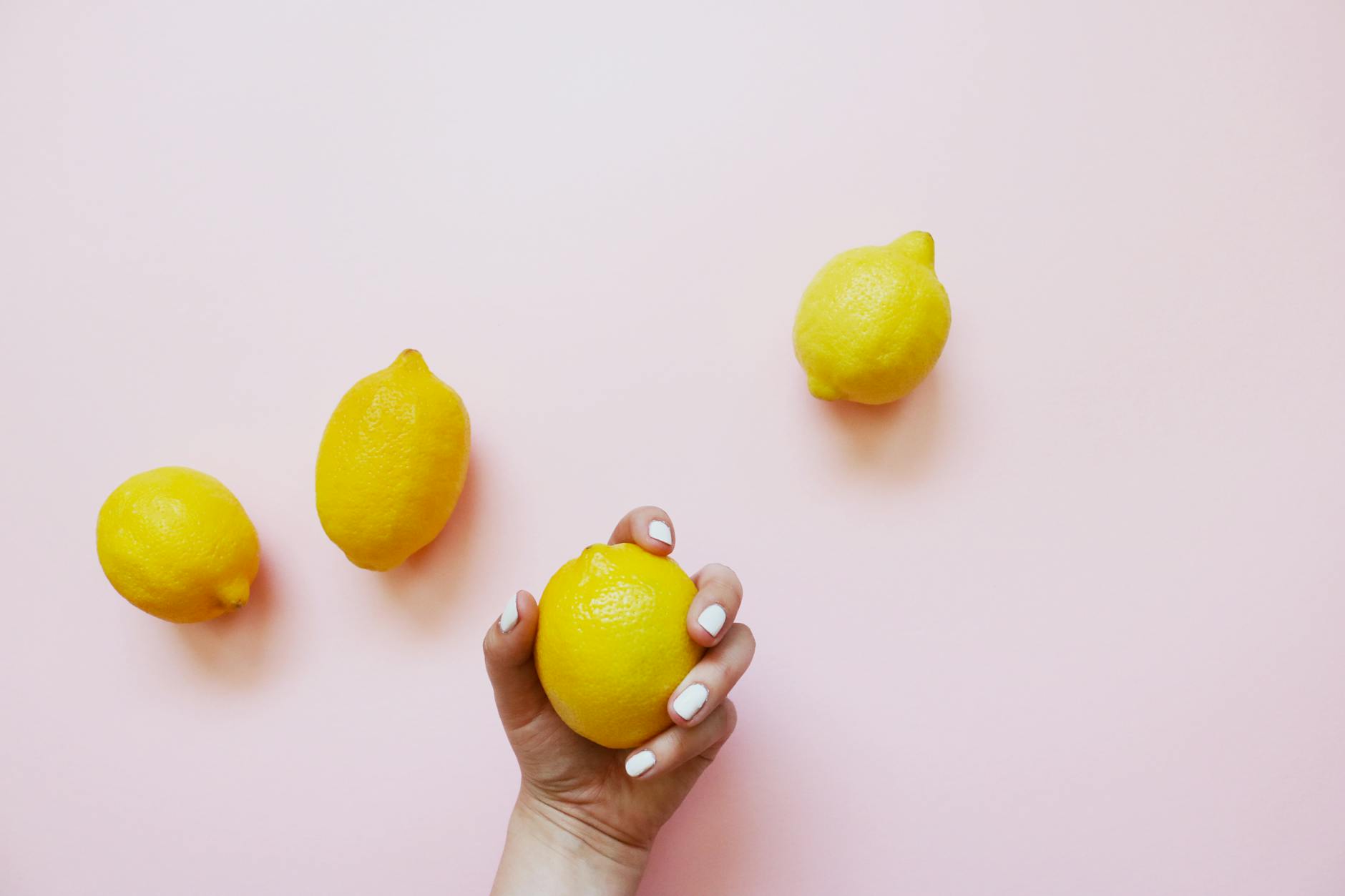 Hand holding fresh lemons on a soft pink background, symbolizing fresh approaches to pleasure exploration