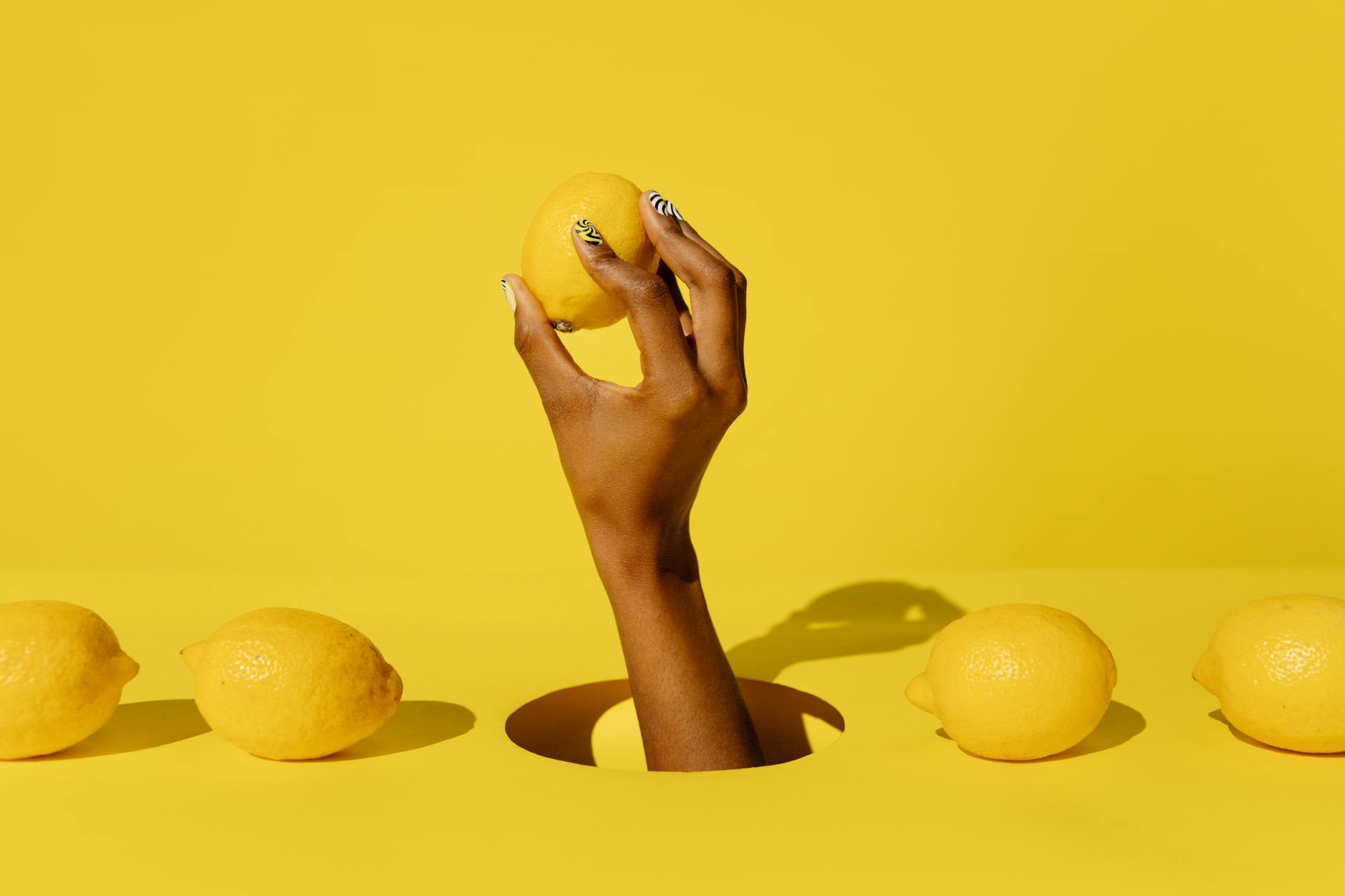 Hand holding a lemon against a bright yellow background, symbolizing fresh sensation and intentional pleasure