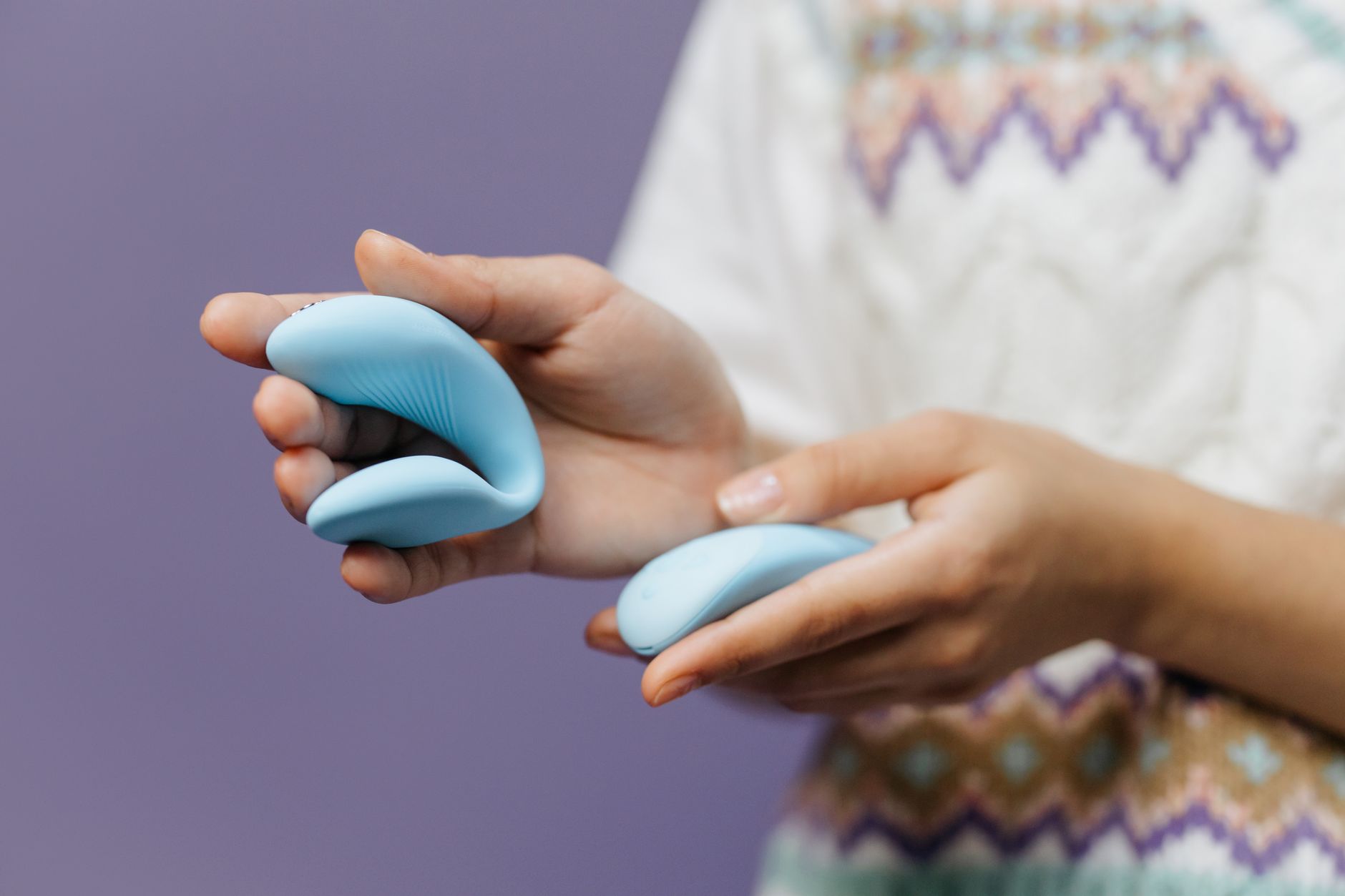 Close-up of hands holding a sleek vibrator against a purple background, representing pleasure restored through intentional tools.