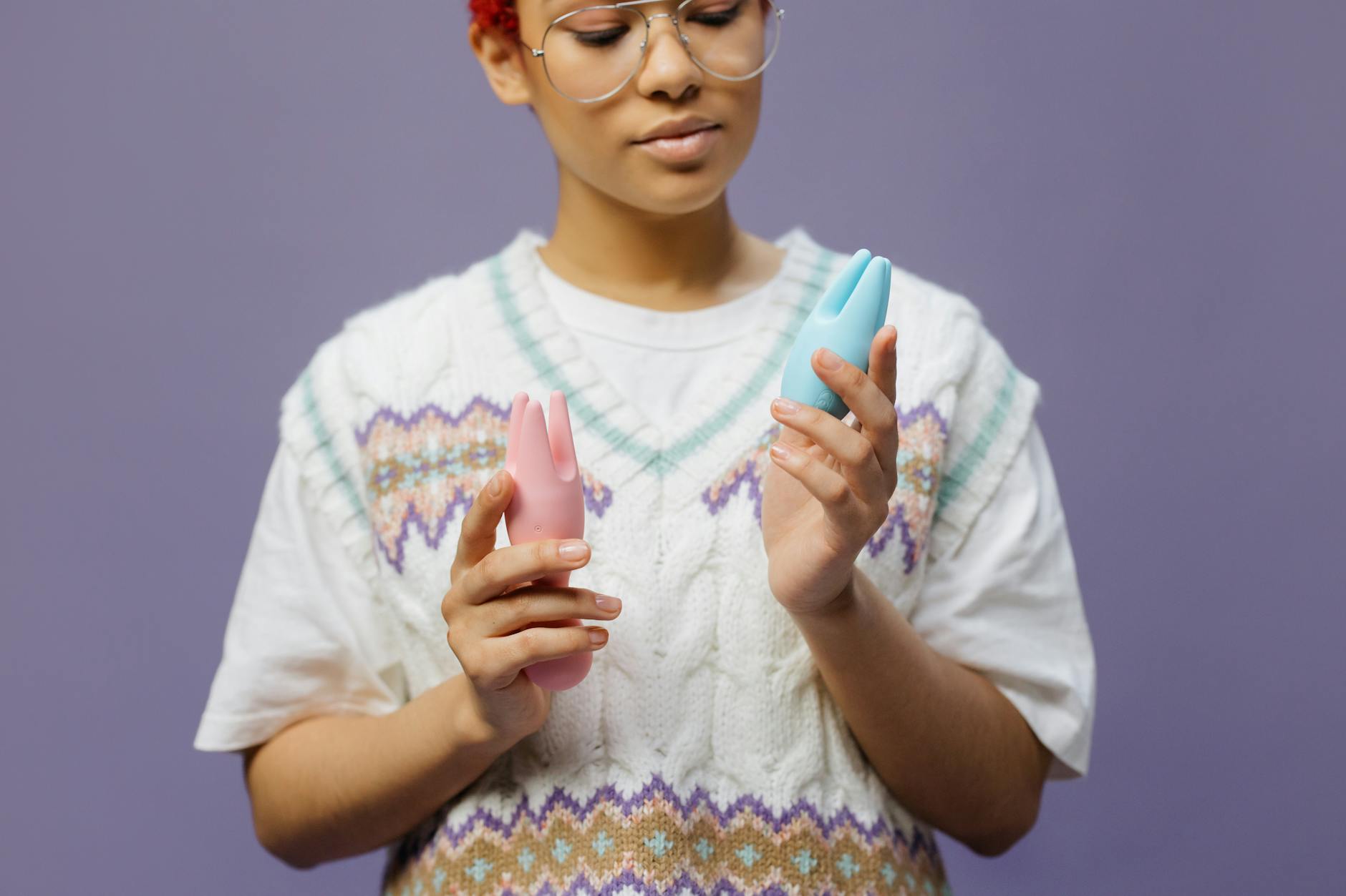 Woman contemplating two colorful vibrators, representing the journey of reconnecting with sensation.
