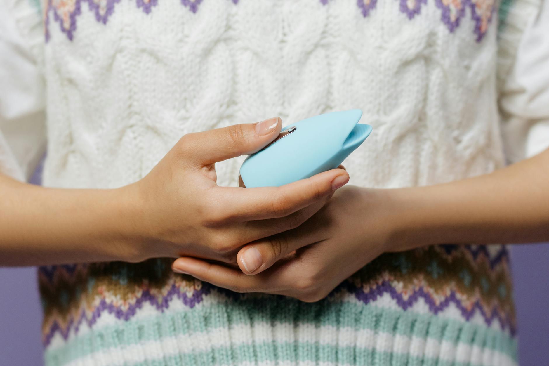 Close-up of hands holding a vibrator together against a knitted sweater, showing intimate partnership.